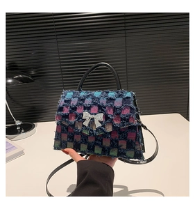 Détail du sac à main en denim à carreaux avec bords effilochés et nœud argenté sur table
