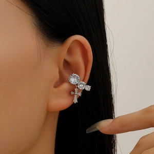 Macro shot of silver ear cuff featuring three zircons and a small cross pendant