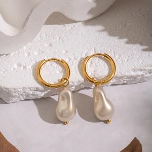 Baroque pearl drop earrings with gold hoop on white textured stone background