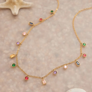 Dettaglio della collana in acciaio inossidabile 18K con zirconi colorati su sfondo di sabbia