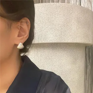 Close-up of silver shell-shaped stud earring with textured surface on female model