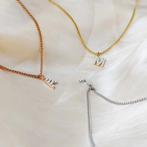 Close-up of three pearl-inlaid initial pendants in gold, silver, and rose gold plating