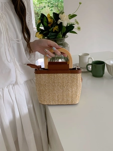 Detail of hand-woven straw bucket bag with dark brown leather trim and wooden handles