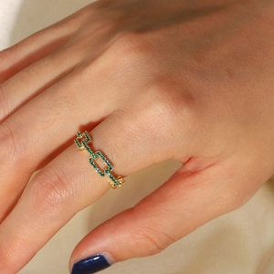 Close-up of gold chain link ring with green zircon micro-pave on a soft beige background