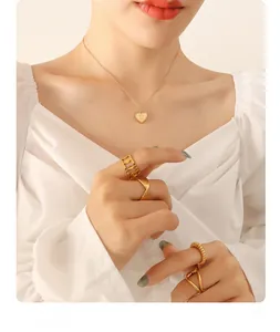 Détail de mannequin portant un collier cœur doré et un ensemble de bagues minimalistes