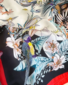 Close-up of silk scarf featuring vibrant tropical parrot and floral print with red borders