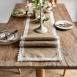 Detail of natural jute table runner with white lace edges on a rustic wooden table