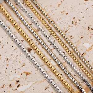 Flat gold and silver stainless steel chain necklaces on a textured stone surface