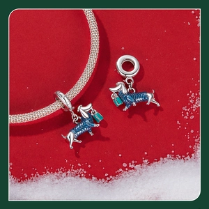 Vue macro d'un charm teckel en argent avec pull émaillé bleu sur fond rouge enneigé