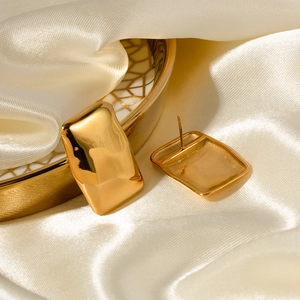 Detailed close-up of gold rectangular stud earrings on elegant silk fabric background