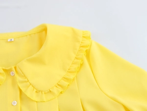 Detail of yellow blouse collar featuring a ruffled Peter Pan neck and small white button
