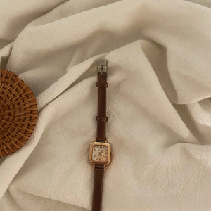 Retro small square women's watch with golden case and brown leather strap on white linen