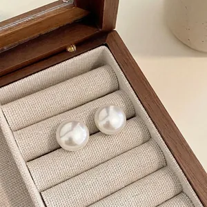 Close-up of minimalist white pearl stud earrings displayed in a wooden jewelry box