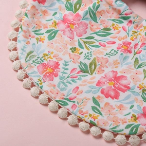Gros plan d'un bavoir floral pour bébé avec bordure à pompons blancs et tissu doux