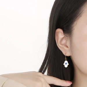 Detailed close-up of a gold Hamsa hand earring with a blue evil eye on a model