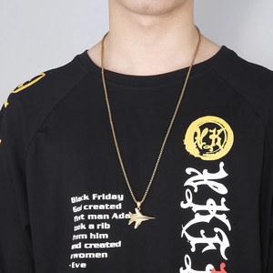 Close-up of a gold fighter jet pendant necklace worn by a model on a black tee