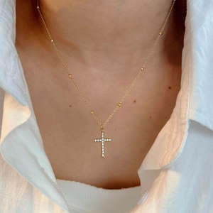 Collier de perles dorées avec pendentif croix en strass porté par un mannequin