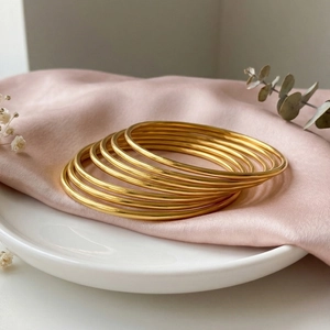 Close-up of 8-10 gold stainless steel bangles stacked on elegant pink silk fabric