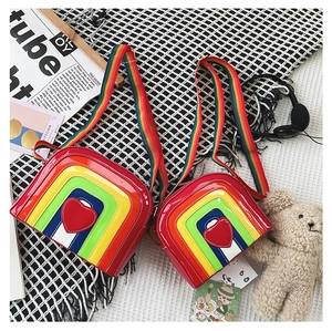 Detail of children's rainbow crossbody bag featuring glossy patent leather and heart patch