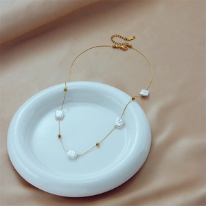 Minimalist gold chain necklace with square pearls and beads on a ceramic plate