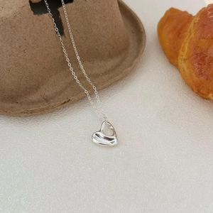 Polished silver heart pendant necklace on minimalist craft paper and croissant background