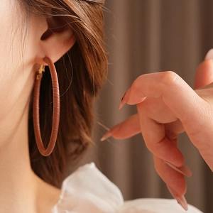 Close-up of model wearing large brown leather texture hoop earrings with gold clasps