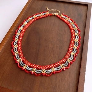 Detail of beaded fan-shaped necklace in red and gold on wooden tray with lobster clasp