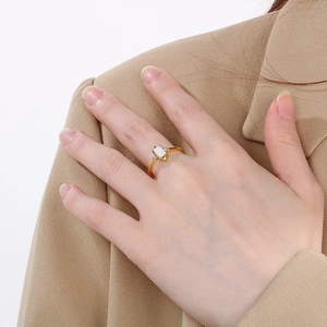 Detail of a gold square opal ring with zircon side stones worn on a finger