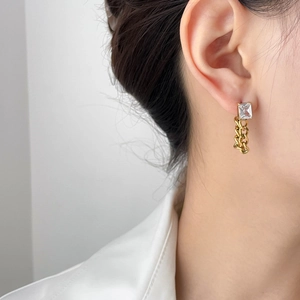 Detailed view of a gold earring with square zircon and thick chain link on model