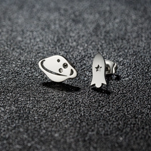 Macro shot of polished silver planet and rocket stud earrings on grey texture
