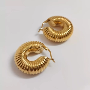 Close-up of golden hollow hoop earrings featuring vertical ribbed texture and plug closure