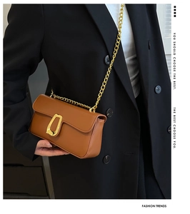 Close-up of brown leather crossbody bag with gold horseshoe buckle on model