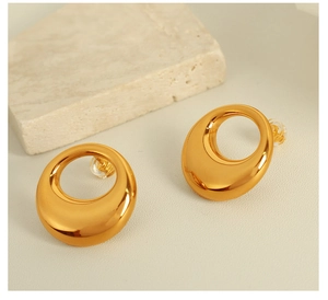 Close-up of golden hollow circle earrings with polished finish on a textured stone base