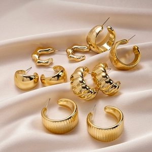 Detailed view of ten gold geometric C-shaped earrings on smooth champagne silk fabric