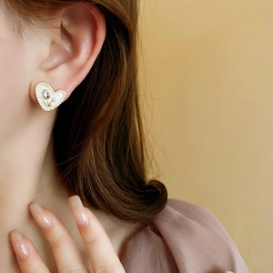 Primo piano di orecchino a cuore bianco con tulipano dorato e perle indossato da modella