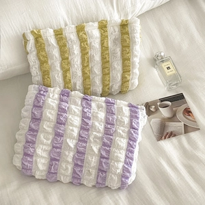 Striped ruffled pillow cosmetic bags in yellow and purple set on a soft white bed