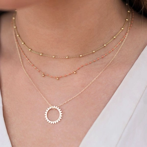 Set di collane dorate a strati con ciondolo a sole e perline corallo su modella