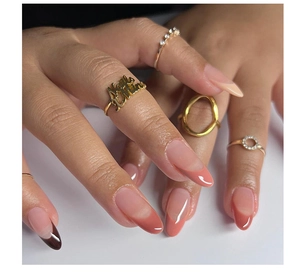 Macro shot of long almond-shaped nails with pink gradient French design and golden rings