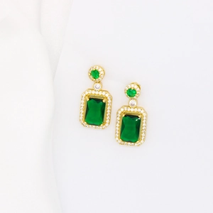 Detailed macro shot of emerald green rectangular drop earrings with gold finish and zircons