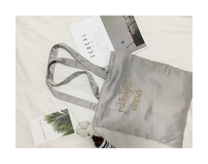 Flat lay of a grey satin tote bag featuring golden midnight circus embroidery and props