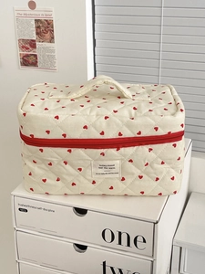 Detail view of quilted cream makeup bag with red hearts and a sturdy top handle