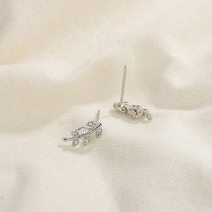 Macro view of silver leaf stud earrings with sparkling cubic zirconia on linen texture