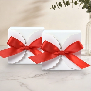 Detail of white gift boxes with red satin bows and scalloped edges on marble