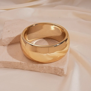 Close-up of wide gold metal bangle resting on stone with silk background texture