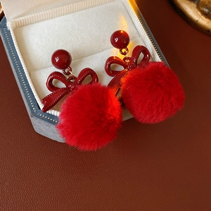 Macro shot of red bow earrings with plush pom-poms presented in a blue jewelry box