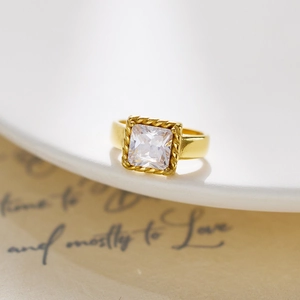 Macro detail of gold-plated ring with square zircon and rope texture border on white ceramic