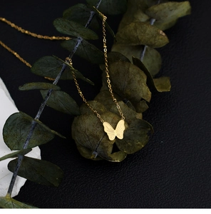 Detailansicht der goldenen 3D-Schmetterlingskette auf Eukalyptusblättern und schwarzem Leder
