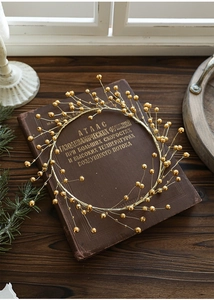 Macro shot of a golden beaded wreath ornament resting on a vintage book for festive decor