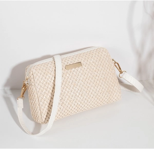Detailed view of beige straw woven crossbody bag with white leather strap and gold hardware