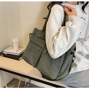 Detail of dark green corduroy tote bag with multiple zippers shown on a model